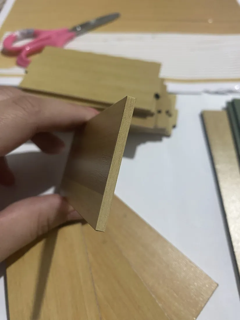 Peças de madeira da maquete abertas em leque sobre a mesa, com as portas verdes ao lado.
