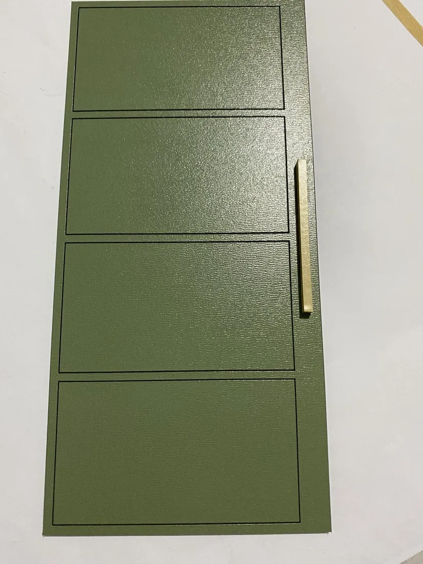 Porta verde da maquete deitada sobre a mesa, com um puxador fino de madeira na lateral.